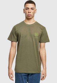 Oliven grøn bomulds t-shirt med rund hals, korte ærmer og et print på venstre bryst, der står "Matcha Iced Latte" i lys grøn.