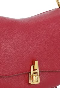 Borsa a mano rossa in pelle con una texture liscia, dotata di una chiusura in metallo dorato e una forma arrotondata. Design minimalista e cuciture ben definite.