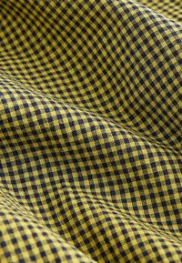 Gewebter Stoff in gelbem und dunkelblauem Karomuster, weiche Textur, mit gleichmäßig verteilten Quadraten und sichtbaren Nahtdetails.