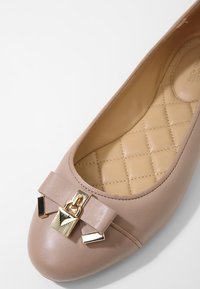 Ballerines en cuir beige clair avec un nœud et des accents en métal doré. Semelle intérieure beige matelassée et design à bout rond. Texture lisse.