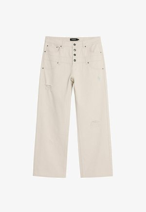 Jean large couleur beige clair en denim, avec une taille haute, cinq poches et des détails usés avec des patchs effilochés.