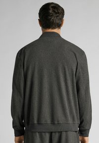 Donkergrijze, getextureerde bomberjack met een ronde kraag; heeft ribgebreide manchetten en een zoom. De achterkant toont een minimalistisch ontwerp en stikseldetails.