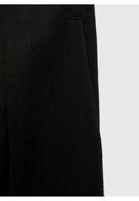 Gros plan d’un tissu noir avec une texture de tissage diagonal visible et une couture verticale sur le côté droit sur un fond gris clair.