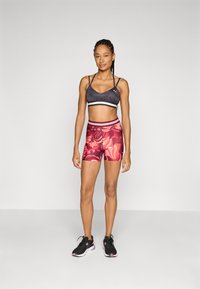 Soutien-gorge de sport noir avec des fines bretelles et une bande blanche, associé à un short à motifs floraux colorés dans des teintes de rose et de rouge, et des baskets noires.