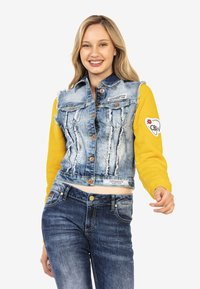 Veste en denim coupée avec finition déchirée et manches longues orange-jaune. Jean bleu avec design classique à cinq poches et fermeture à bouton.