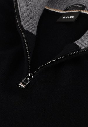 Zwarte trui met een ritssluiting, grijze ribgebreide kraag en een metalen rits met een merkgetrokken. Zacht kasjmiermateriaal.