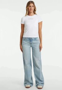 Bílá bavlněná tričko s potiskem "GUESS JEANS", spárované s lehce modrými širokými denimovými džínami s vybledlým umytím a klasickým pětipocketovým designem.