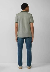 Grünes Poloshirt mit dunkelgrünen Akzenten, kurzen Ärmeln und strukturierter Oberfläche, kombiniert mit blauen Jeans und hellen Schuhen.