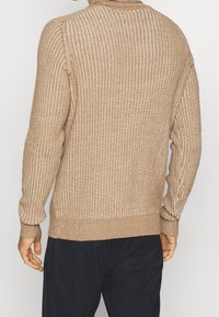 Beige geribbelde trui met een hoge kraag en lange mouwen. Heeft een getextureerde brei en aangesloten manchetten en zoom. Eenvoudig ontwerp, zonder zichtbare patronen.