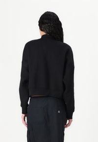 Musta lyhyt collegepaita pyöreällä pääntiellä ja leveillä hihoilla, valmistettu pehmeästä materiaalista, jossa on resorit hihansuissa ja helmassa.