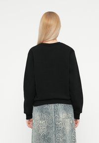 Zwarte sweatshirt met lange mouwen, geribbelde manchetten en zoom, gecombineerd met een lichtblauwe rok met een slangenleerpatroon.
