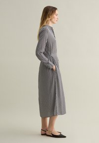 Long-sleeve black and white polka dot dress with a tie waist, two side pockets, and black flats featuring a gold accent. Smooth fabric texture.