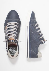 Niebieskie skórzane trampki z szarymi akcentami, posiadające perforowane boki, białe podeszwy i szare sznurowadła. Wnętrze ma strukturalny wzór.