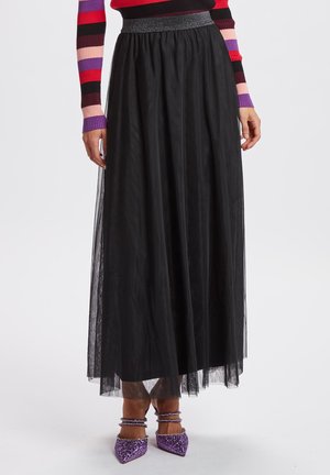 Femme portant une longue jupe en tulle noire avec une ceinture scintillante, un haut rayé à manches longues et des talons à bride cheville pailletés violets.