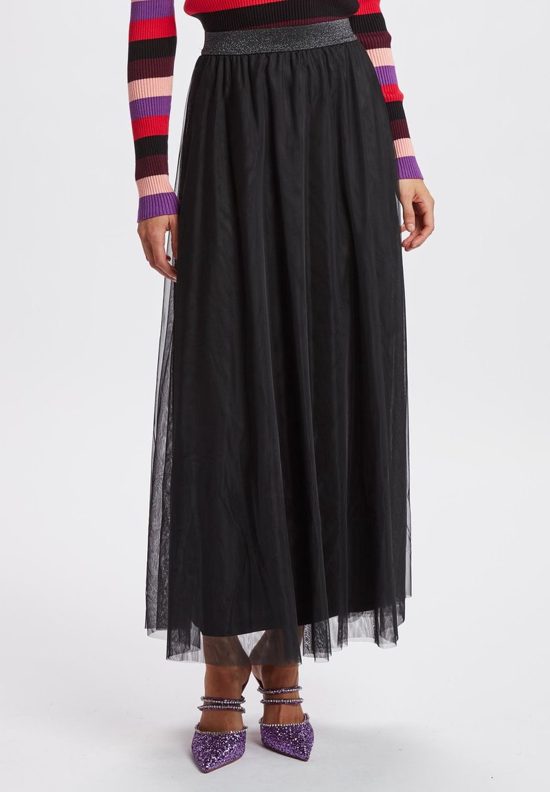 Femme portant une longue jupe en tulle noire avec une ceinture scintillante, un haut rayé à manches longues et des talons à bride cheville pailletés violets.