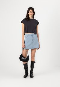 T-shirt noir court, jupe en denim bleu clair, bottes noires jusqu'aux genoux et un sac à main noir avec lettrage argenté et bandoulière en chaîne.