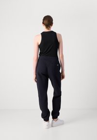 Čierny rebrovaný tielko spárované s tmavomodrými teplákmi s elastickým pásom a manžetami na členkoch. Biele tenisky dotvárajú outfit.