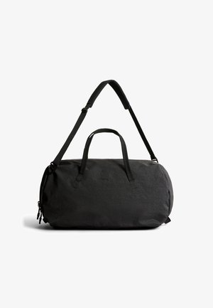 Sac de sport en tissu noir doux avec deux poignées et une bandoulière rembourrée réglable, présenté sur un fond blanc.