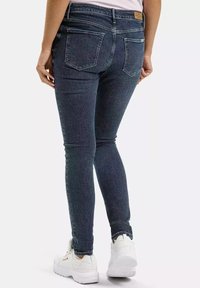 Slimowane ciemnoniebieskie dżinsy z średnim stanem, twoimi tylnymi kieszeniami i subtelnymi detalami przeszycia, zestawione z białymi trampkami.