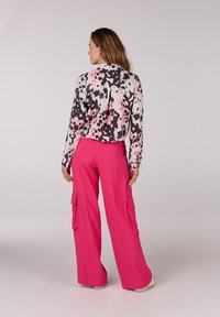 Langdurige blouse met een zwart-wit abstract bloempatroon, gecombineerd met felroze cargobroek met zijzakken.