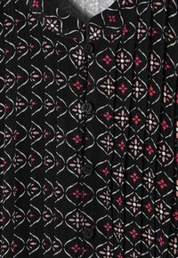 Blusa nera plissettata con un motivo floreale e geometrico in rosa, bianco e azzurro chiaro. Bottoni neri adornano la chiusura.