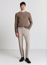 Maglione marrone a maglia con motivo testurizzato, pantaloni beige su misura e stivali in pelle nera. Vestibilità slim e palette di colori neutri.