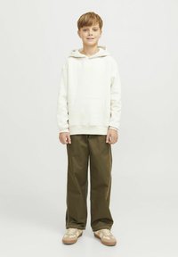 Sudadera blanca con capucha y bolsillo delantero, combinada con pantalones de pierna ancha en verde oliva y zapatillas beige con un diseño ligero.