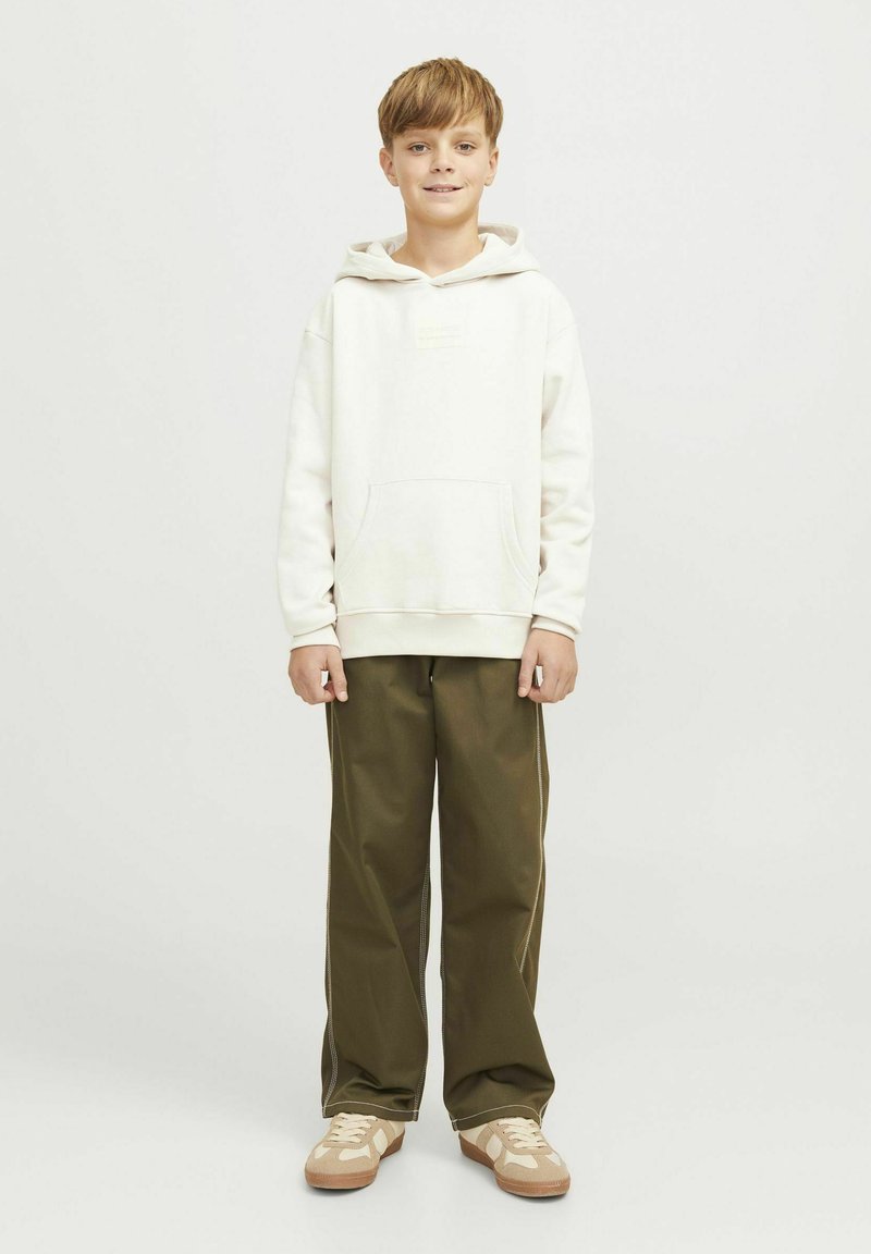 Sudadera blanca con capucha y bolsillo delantero, combinada con pantalones de pierna ancha en verde oliva y zapatillas beige con un diseño ligero.
