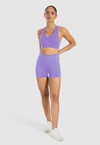 Paarse geribbelde sportbeha en bijpassende shorts met hoge taille van rekbare stof. Witte sportschoenen maken de outfit compleet.