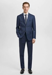 Navy blue tailored suit made of smooth fabric; two-button jacket with notch lapels, flat-front trousers, paired with a textured tie and black shoes.