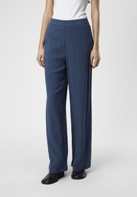 Pantalons tailleur bleus à coupe droite et texture subtile, dotés d'une taille haute et d'une finition lisse, associés à des bottines noires.