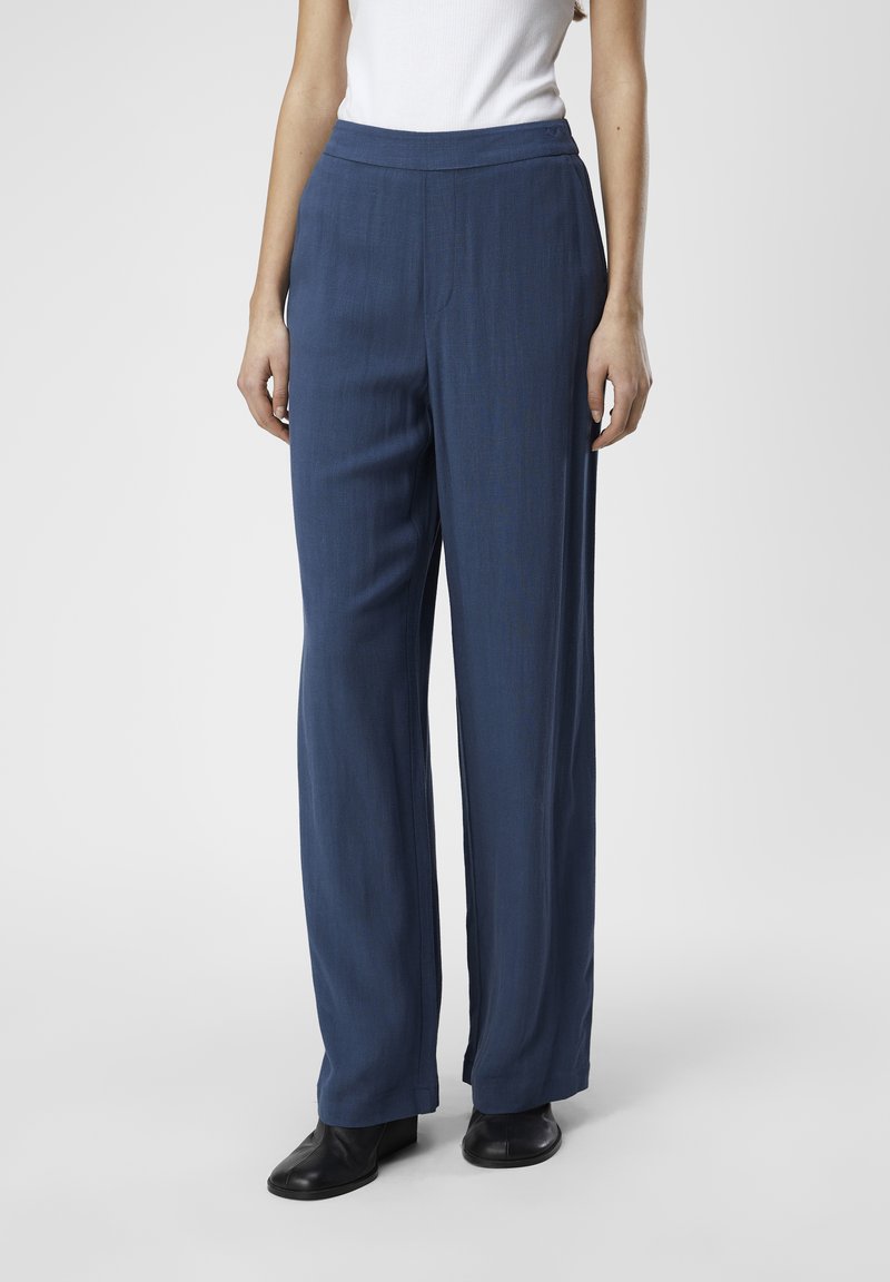 Pantalons tailleur bleus à coupe droite et texture subtile, dotés d'une taille haute et d'une finition lisse, associés à des bottines noires.
