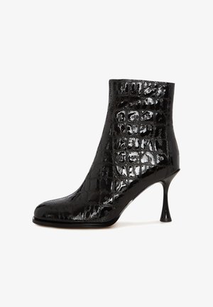 Stivale alla caviglia nero con una finitura lucida e una texture a coccodrillo, punta affusolata e un tacco a stiletto unico. Realizzato in materiale sintetico.