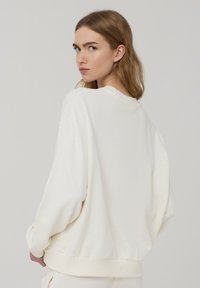 Felpa oversize di colore crema realizzata in morbido tessuto, con scollatura rotonda, cuciture delle spalle scese e polsini e orlo a coste.