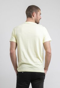 T-shirt jaune clair à manches courtes avec un col rond, texture douce et coupe décontractée, porté avec un pantalon noir. Design minimaliste sans motifs.