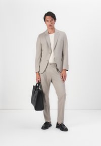 Light gray suit with a single-breasted jacket, elastic waistband trousers, and a cream t-shirt. Black leather bag and shoes complete the outfit.