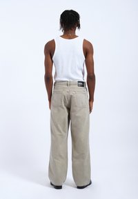 Helle graue, lässige Jeans mit hoher Taille und zwei Gesäßtaschen, getragen mit einem weißen Tanktop. Schlichte Stoffqualität, minimale Akzente.