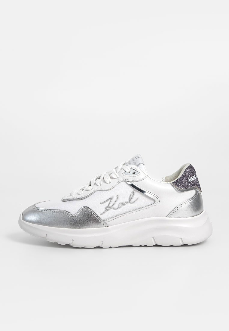 Des chaussures de sport blanches avec des accents argentés, présentant un dessus texturé, un bout rond, une semelle plate en caoutchouc et un petit logo sur le côté.
