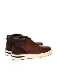 Bruine leren en suède hoge schoenen met een witte rubberen zool, voorzien van zwarte accentstrepen en veters, en een ritsafsluiting.