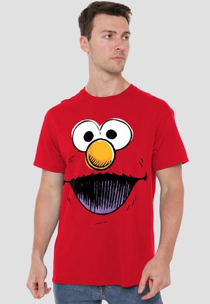 Red cotton T-shirt featuring a large cartoon face with prominent eyes, orange nose, and purple mouth; short sleeves, crew neck design.