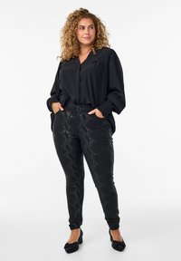 Crna bluzica s V izrezom i širokim rukavima, u kombinaciji s crnim skinny trapericama s uzorkom zmijske kože. Crne cipele s teksturom zaokružuju cijeli outfit.