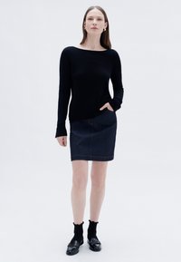 Schwarzer langärmeliger Pullover mit weitem Ausschnitt, kombiniert mit einem dunkelblauen Bleistiftrock aus Denim, der über eine Fronttasche und helle Nähte verfügt.