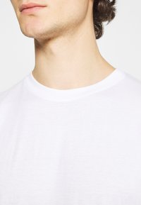 T-shirt en coton blanc avec un col rond. Texture douce et lisse, couture visible autour du col, et un design simple et classique.