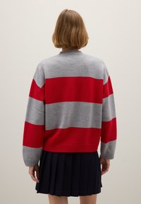 Maglione a righe grigie e rosse con scollo rotondo e maniche lunghe, realizzato in un morbido materiale a maglia. Abbinato a una gonna plissettata blu navy.