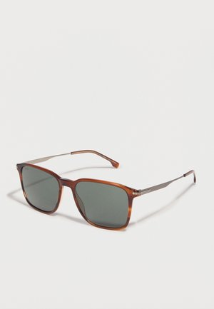 Lunettes de soleil rectangulaires marron avec des verres vert foncé et des branches métalliques fines, présentées sur un fond blanc.