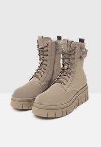 Bottines en daim beige à plateforme épaisse, avec des lacets, une fermeture éclair sur le côté et une languette de boucle pour un enfilage facile.