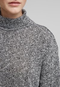 Grå och vit stickad turtleneck-tröja med ett texturerat mönster och ribbat halslinning, som visar upp en mysig, lager-på-lager-design.