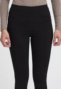 Černé elastické kalhoty s vysokým pasem, mají dvě přední kapsy a hladký povrch. Jednoduchý design bez viditelného kovového vybavení nebo vzorů.