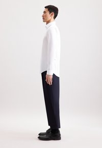Witte langemouwen shirt, slim fit, gecombineerd met marineblauwe broek en zwarte schoenen. Glad materiaal met knoopmanchetten en een ronde zoom.