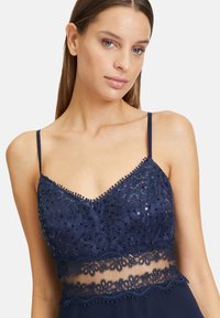 Robe marine avec un décolleté en V et des bretelles fines, ornée de sequins et de dentelle au niveau de la taille. Texture de tissu lisse.